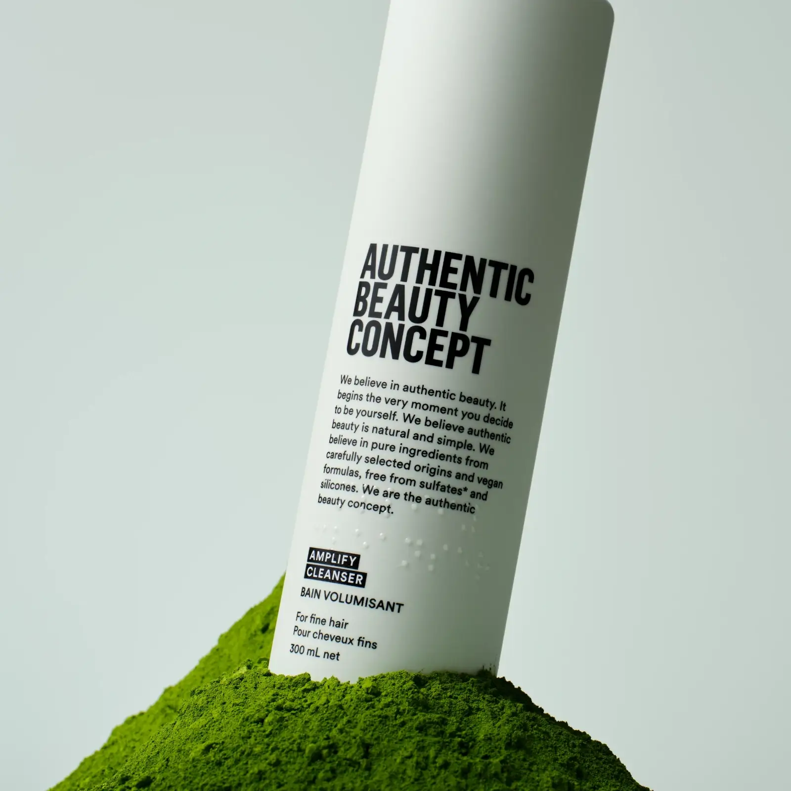 Authentic Beauty Concept Amplify cleanser 300ml bottle stood in a mound of green matcha powder