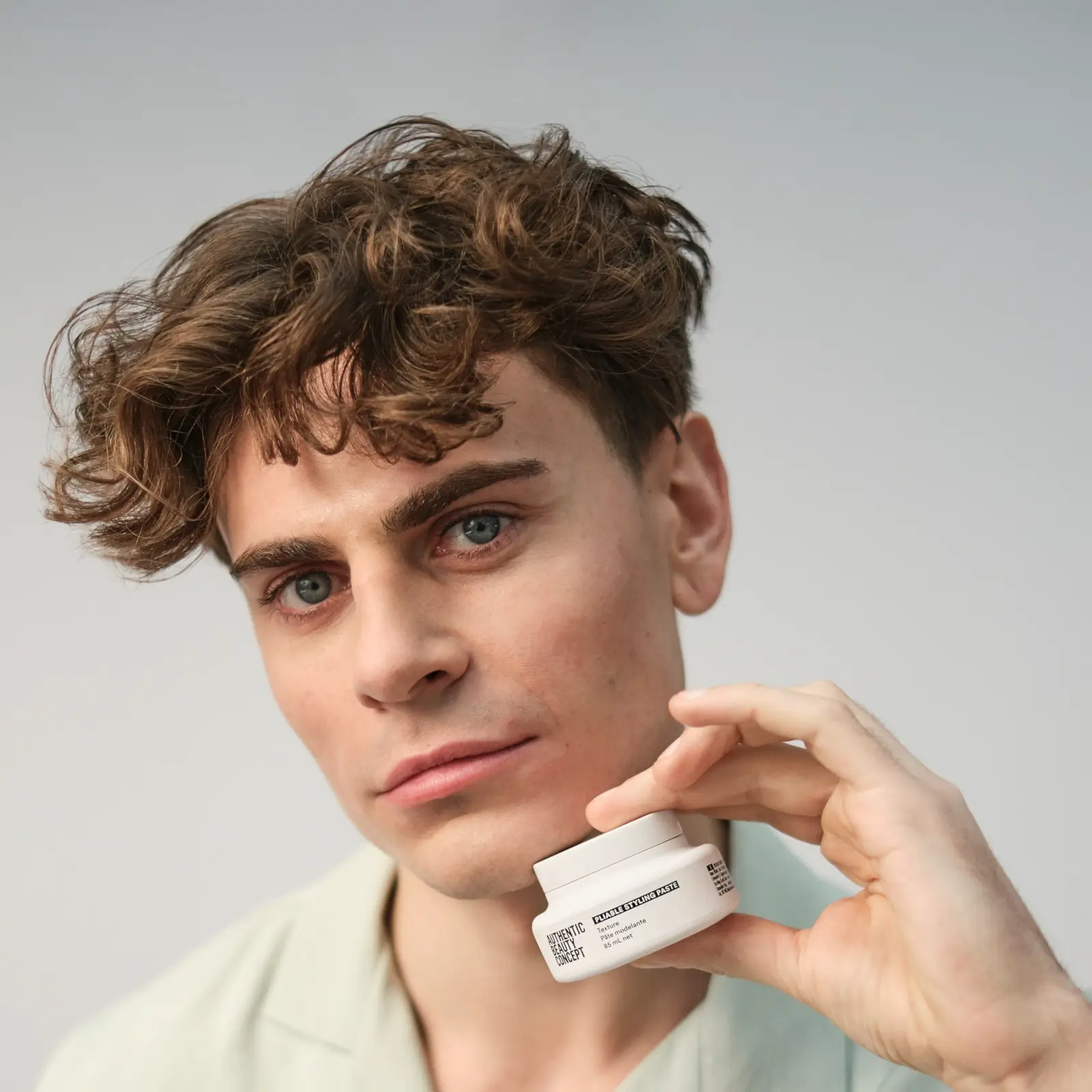 Male with short wavy hair holding a pot of authentic beauty concept pliable styling paste