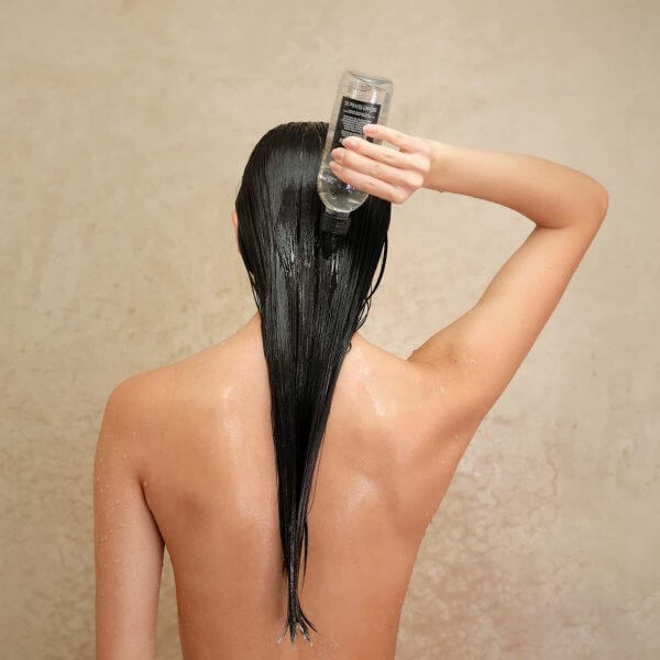 Photo showing hair model applying Davines Oi Liquid Luster in the shower by squeezing liquid onto hair